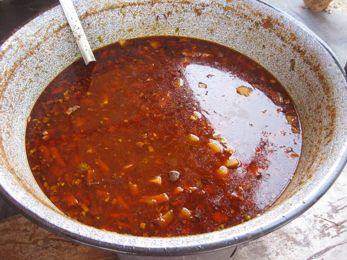 Een grote ketel met dampende Hongaarse goulashsoep vol paprika, wortel en stukjes vlees, met een pollepel erin