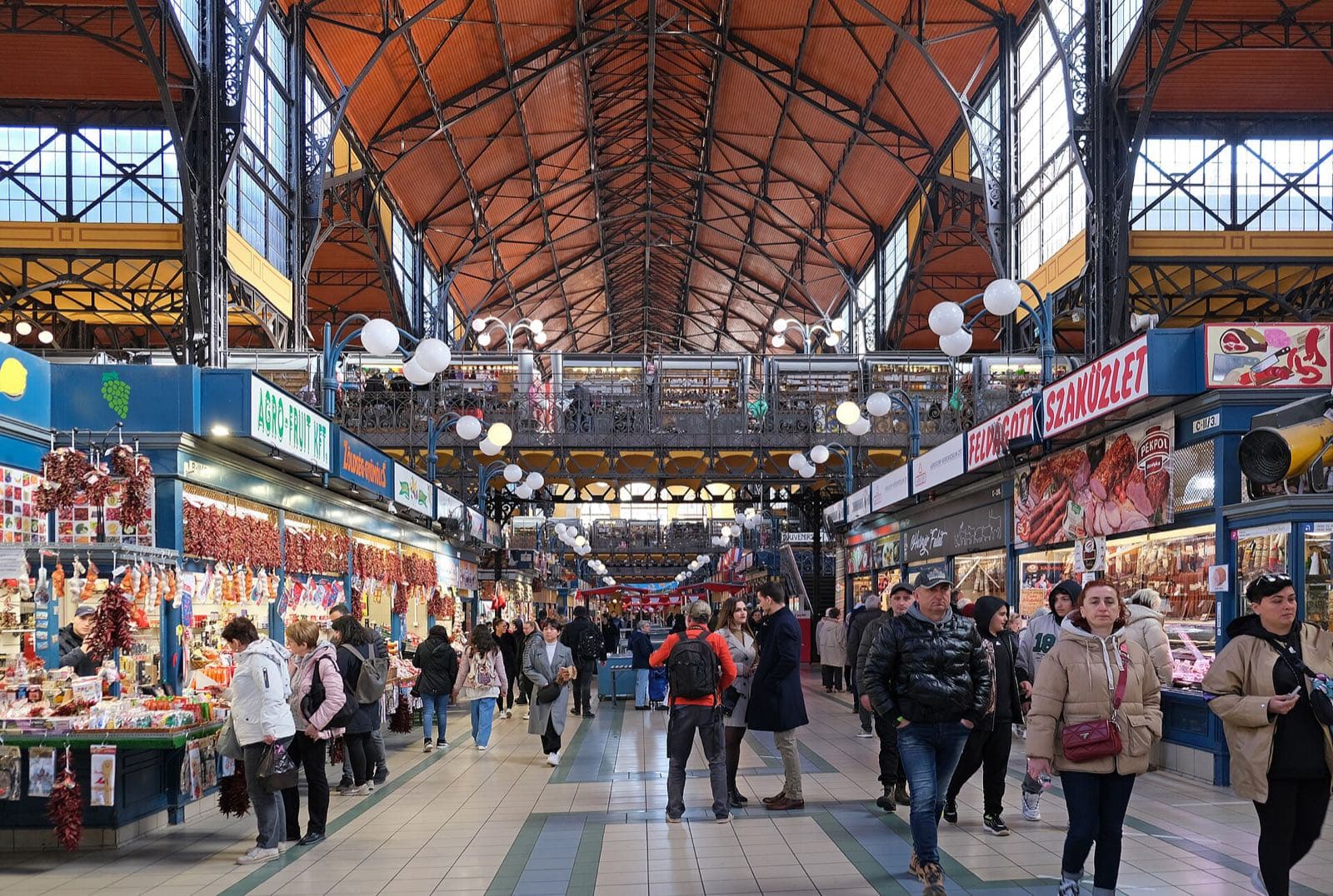 Het interieur van de Grote Markthal met rijen kraampjes vol paprika's en worst, bezoekers en het ijzeren dakgebinte