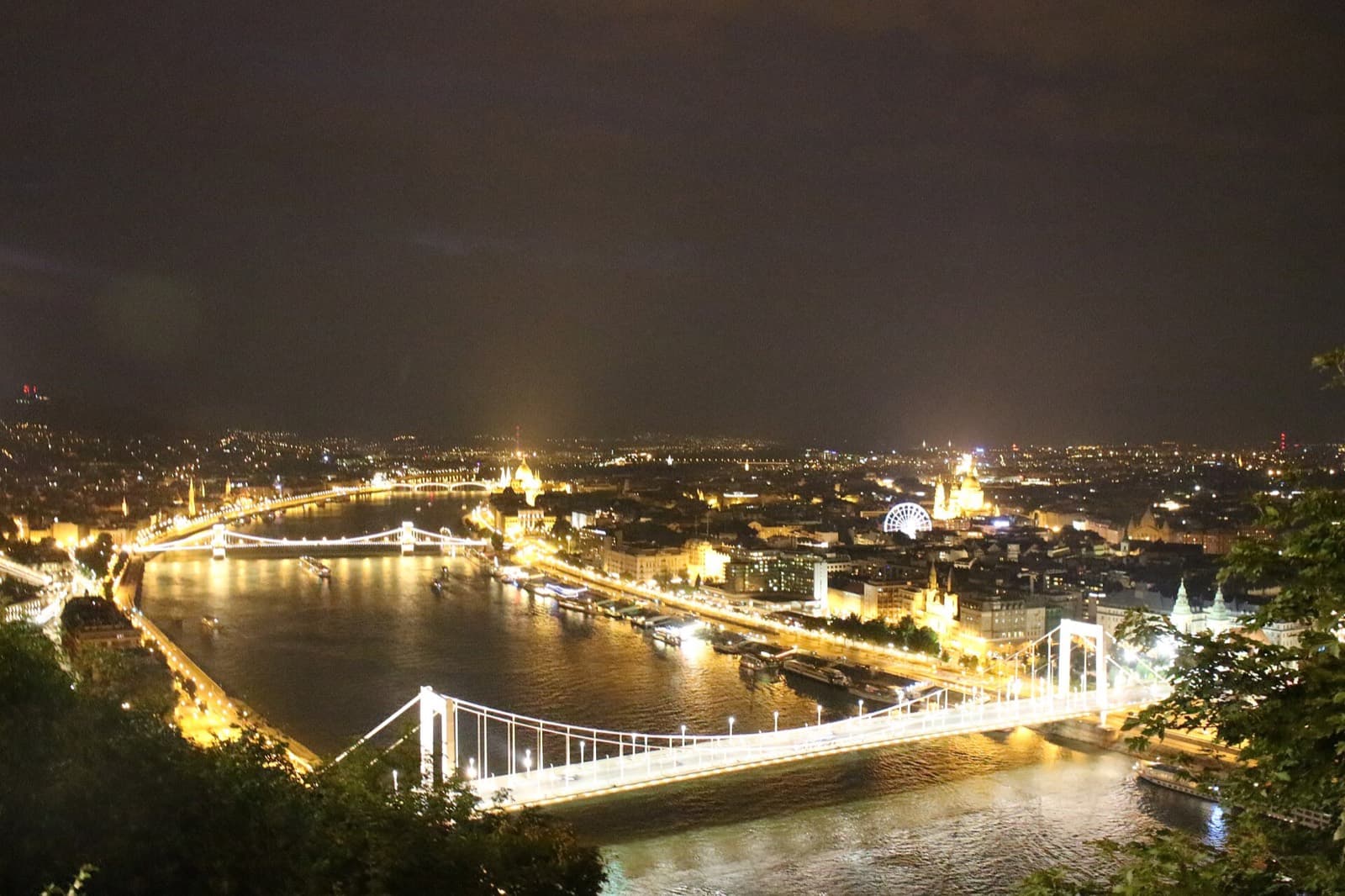 Nachtelijk uitzicht vanaf de Gellértheuvel over de verlichte Donau met de witte Elisabethbrug op de voorgrond, de Kettingbrug, het Parlement en de Sint-Stefanusbasiliek in de verte