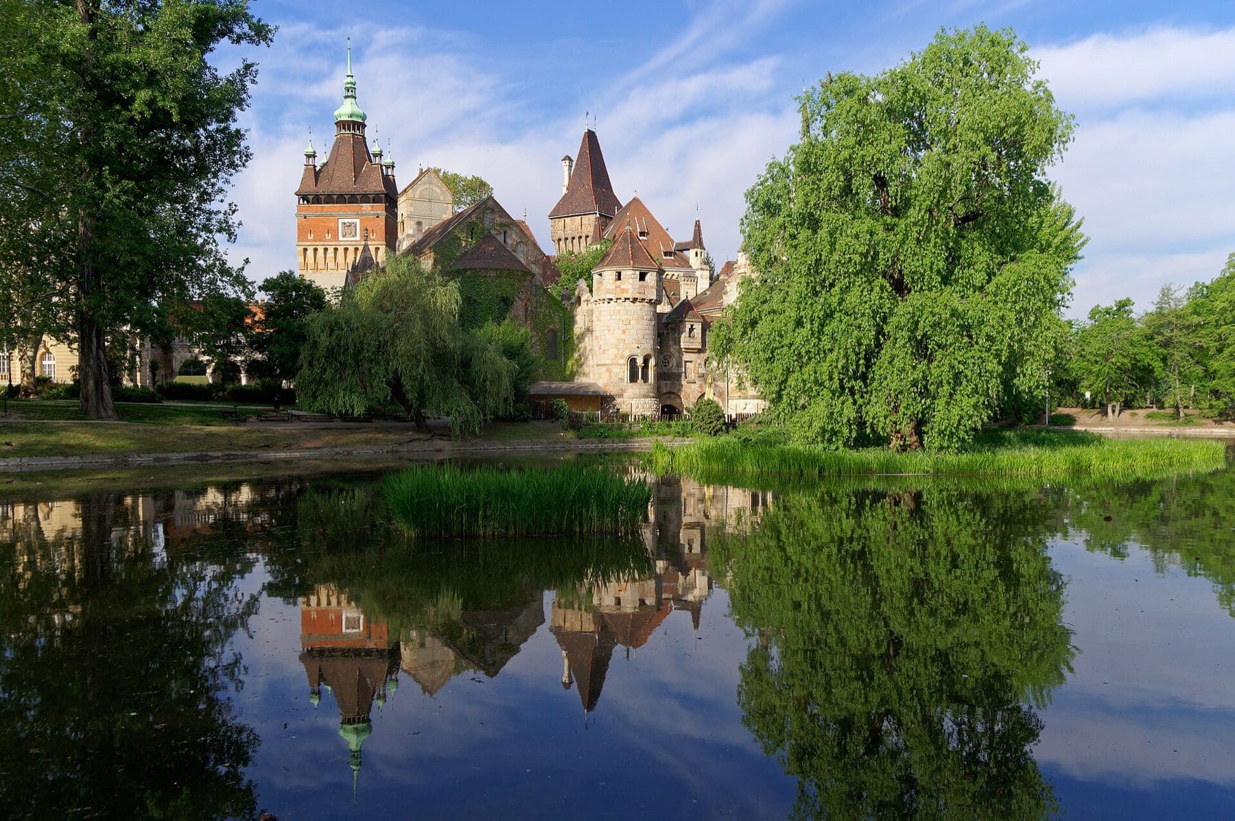 Kasteel Vajdahunyad in het Stadspark met torens en spitse daken, weerspiegeld in de vijver tussen groene treurwilgen